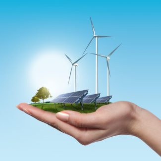 Wind turbines and solar panels on meadow with tree holds in womans hand against blue sky and clouds. Green energy concept